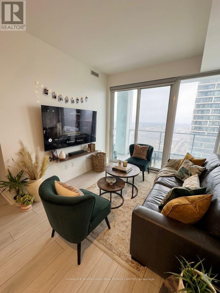 A living room with a green armchair, a brown leather couch, and a flat screen TV mounted on the wall.