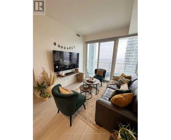 A living room with a green armchair, a brown leather couch, and a flat screen TV mounted on the wall.
