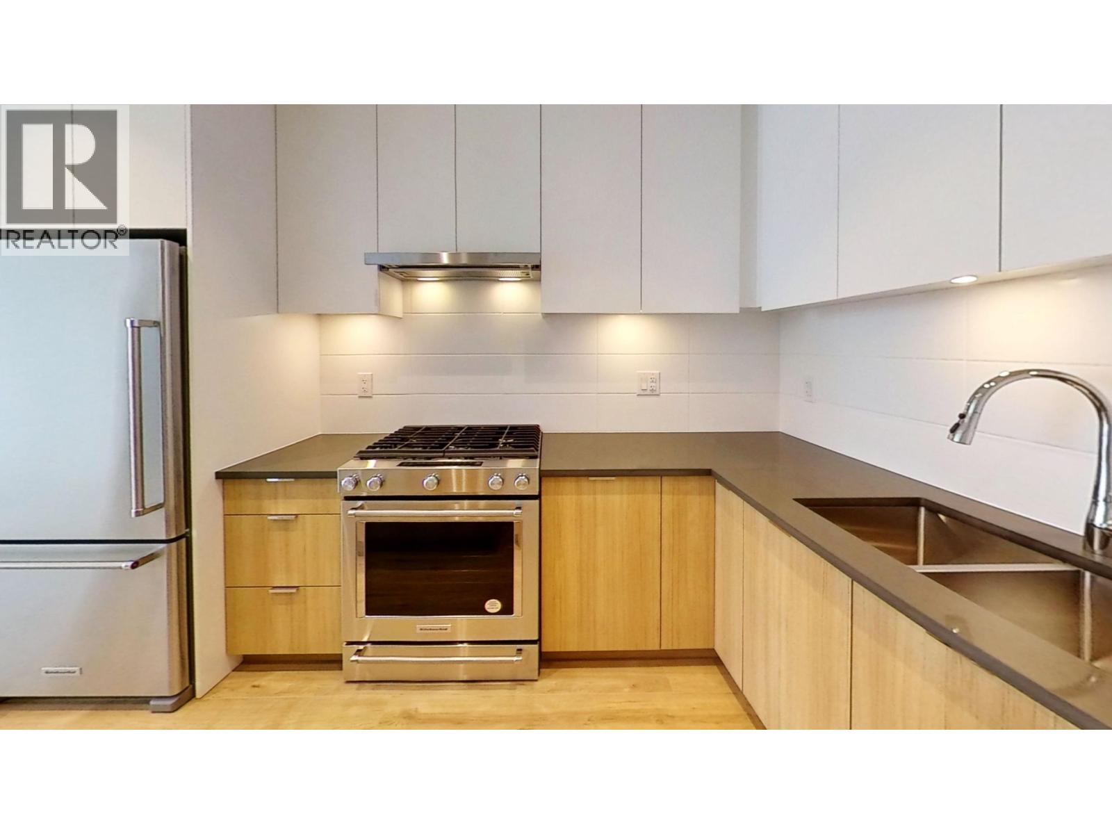 A kitchen with a stainless steel refrigerator, oven, and sink.