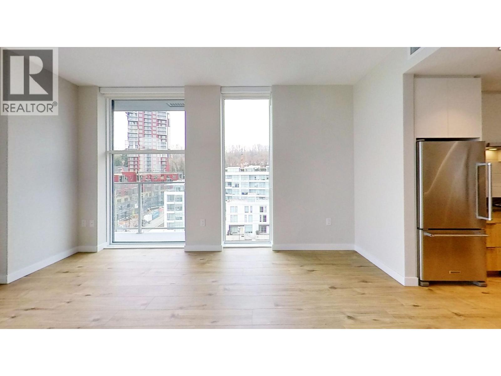 A large empty room with a wooden floor and a refrigerator on the right side.