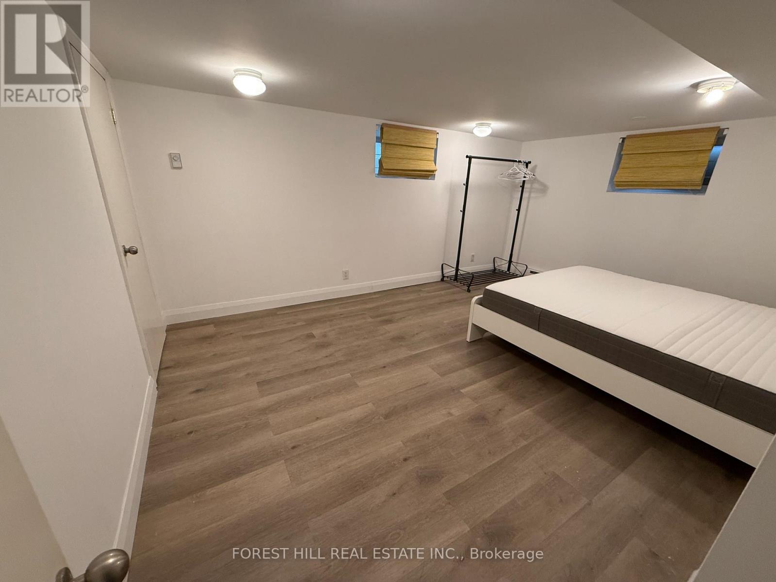 A bedroom with a bed, wooden floor, and a window with yellow blinds.
