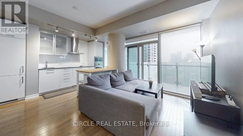 A modern living room with a grey couch and a kitchen area in the background.