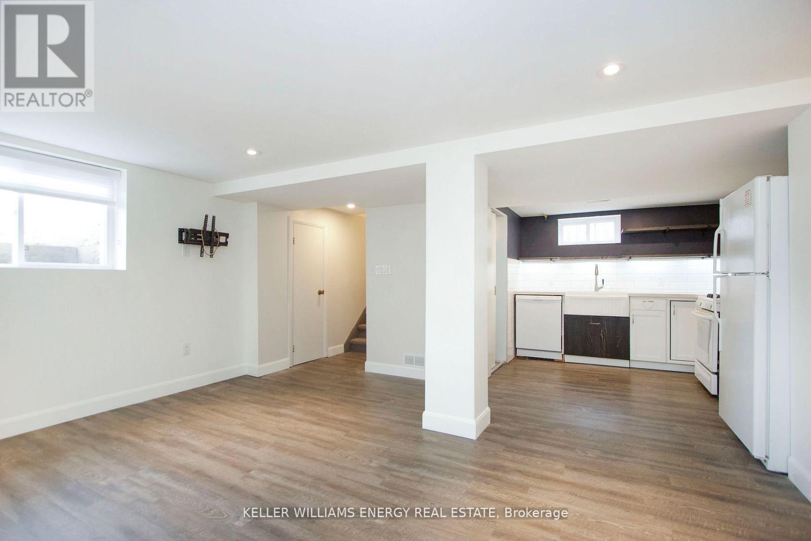 A spacious room with wooden floors and white walls, with a kitchen area visible in the background.
