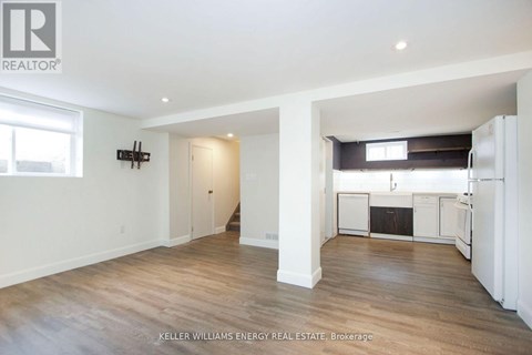 A spacious room with wooden floors and white walls, with a kitchen area visible in the background.