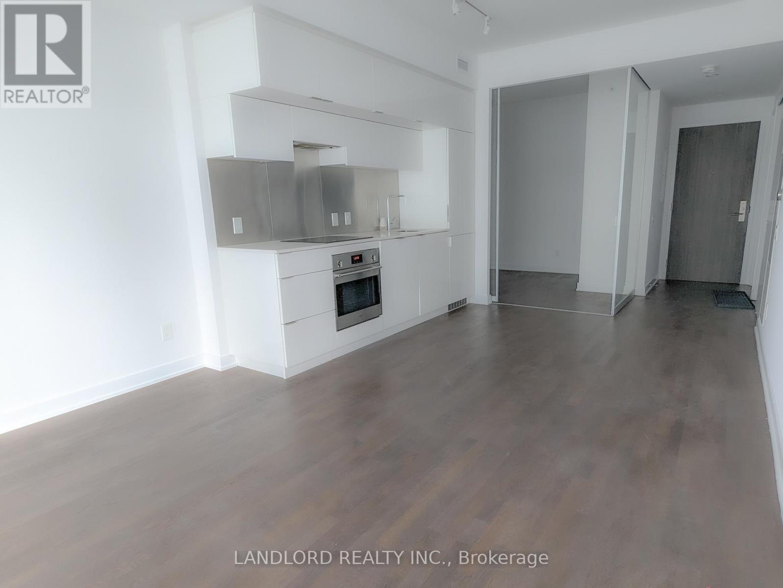 A spacious room with wooden flooring and a built-in stainless steel range hood.