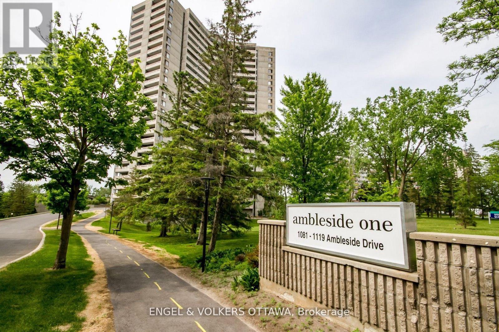 A sign for Ambleside One is in front of a building and trees.