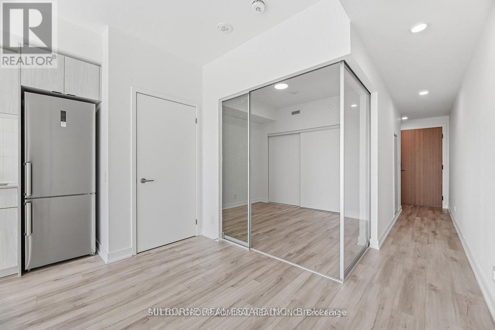 A spacious, empty room with a refrigerator and a mirror on the wall.