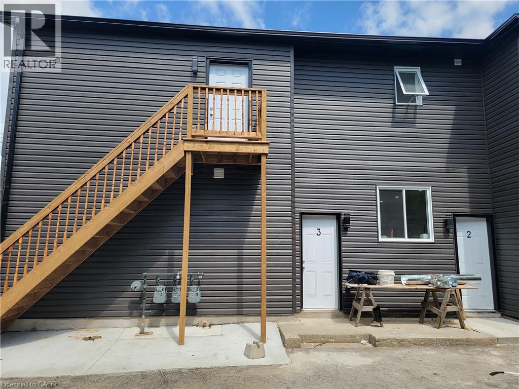 A wooden staircase leads to a balcony on the second floor of a grey house.