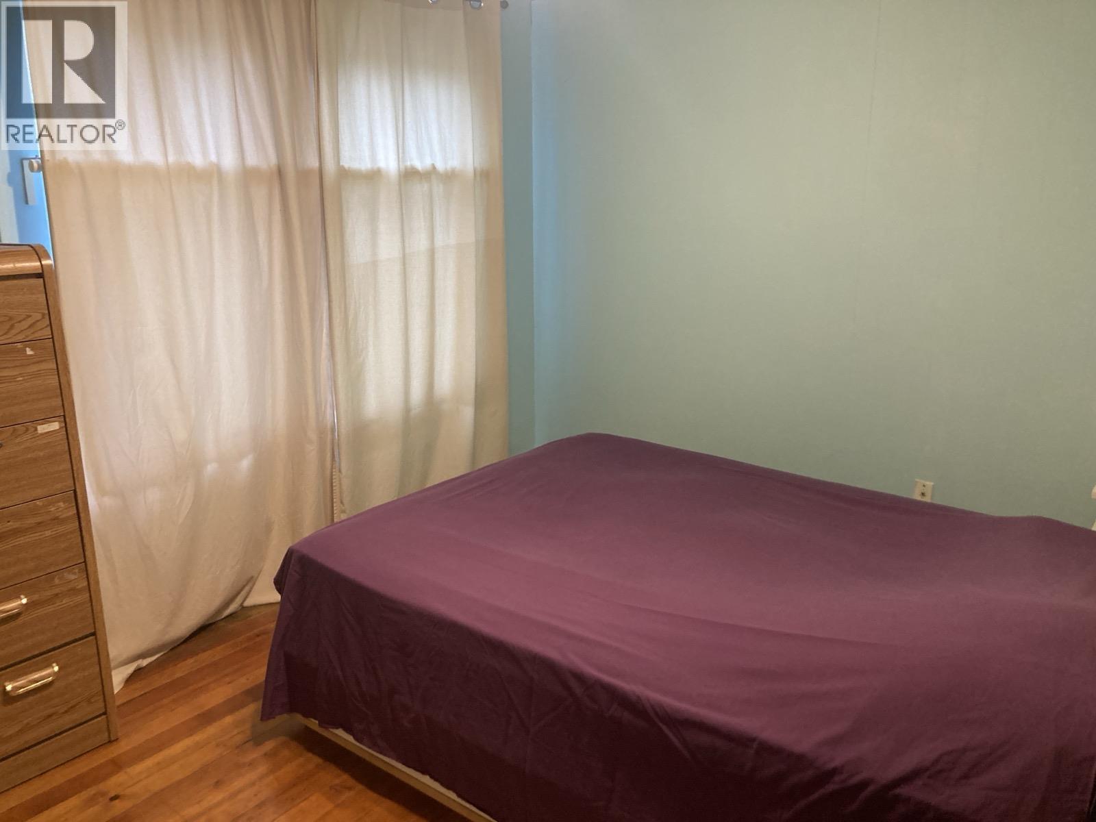 A bedroom with a purple bedspread and a wooden dresser.