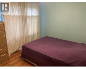 A bedroom with a purple bedspread and a wooden dresser.