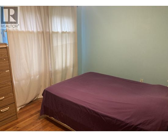 A bedroom with a purple bedspread and a wooden dresser.