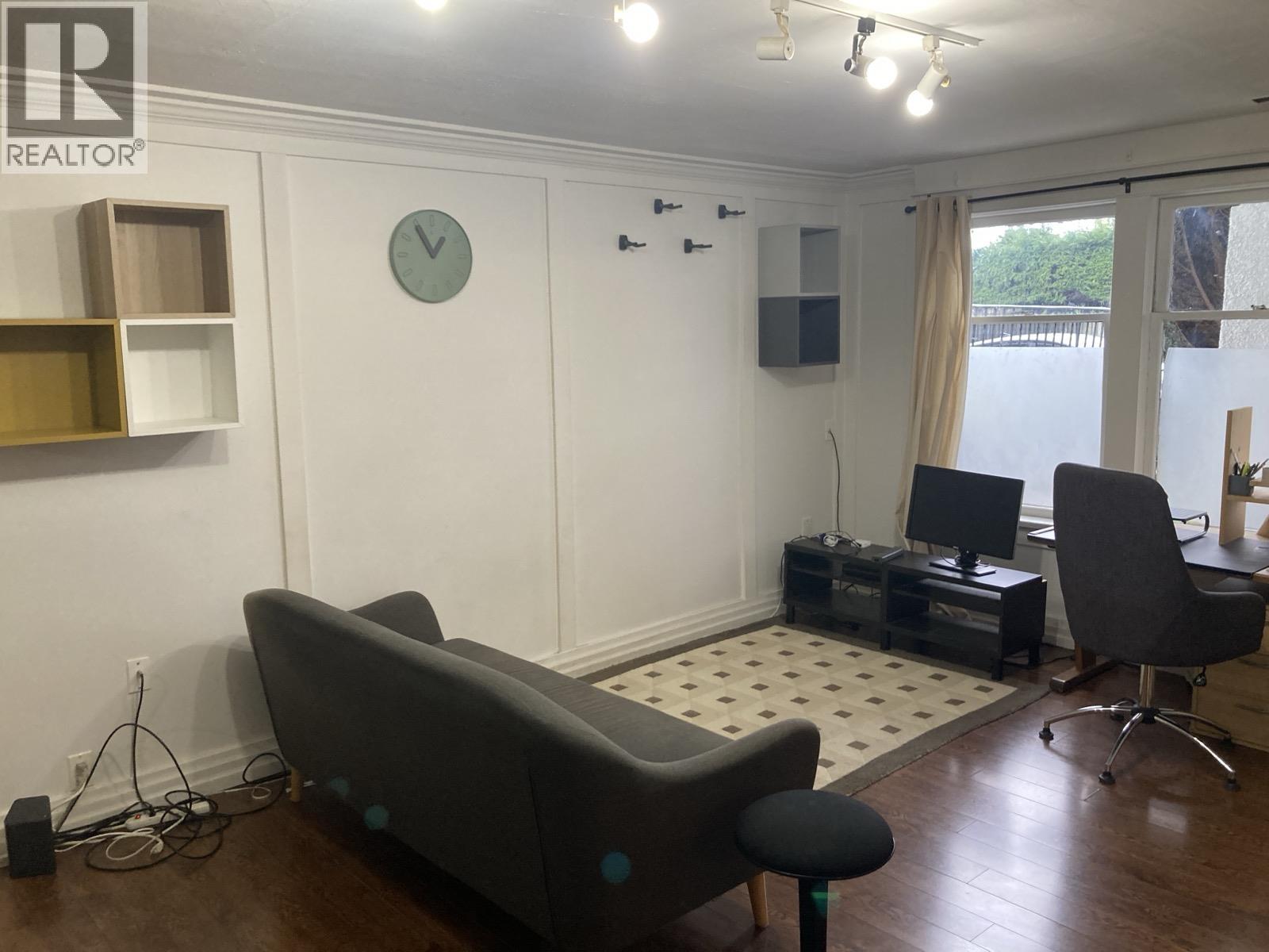 A living room with a grey couch, a black chair, and a white clock on the wall.
