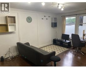 A living room with a grey couch, a black chair, and a white clock on the wall.