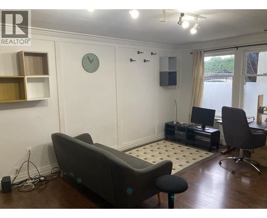 A living room with a grey couch, a black chair, and a white clock on the wall.