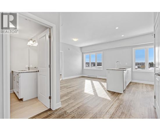 A realtor photo of a white kitchen with wood floors and a view of the outdoors through the windows.