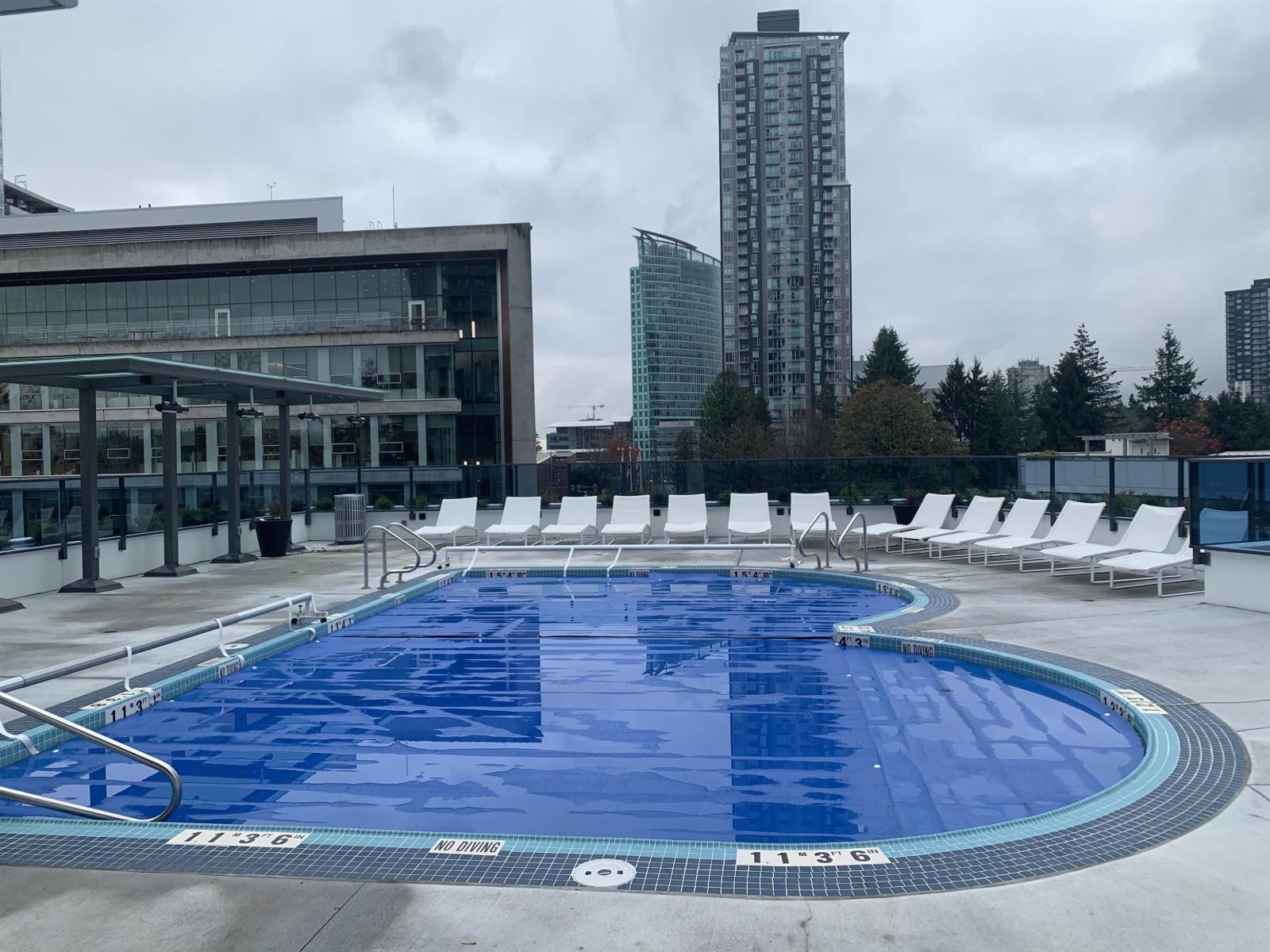 A large blue swimming pool with white lounge chairs and a building in the background.