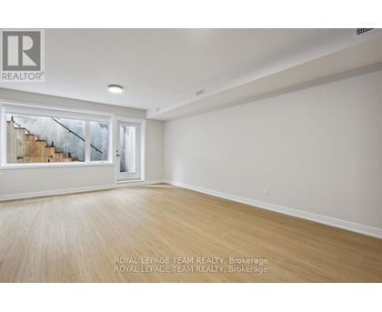 A spacious room with wooden flooring and a large window overlooking a staircase.