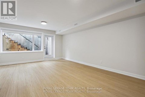 A spacious room with wooden flooring and a large window overlooking a staircase.
