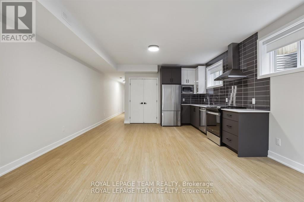 A kitchen with white cabinets and a white refrigerator in a room with wooden floors and white walls.