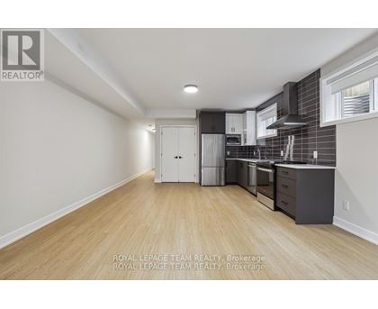 A kitchen with white cabinets and a white refrigerator in a room with wooden floors and white walls.