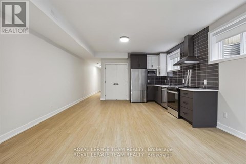 A kitchen with white cabinets and a white refrigerator in a room with wooden floors and white walls.