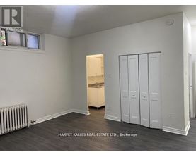 A room with a white wall and a wooden floor with a cabinet and a drawer.