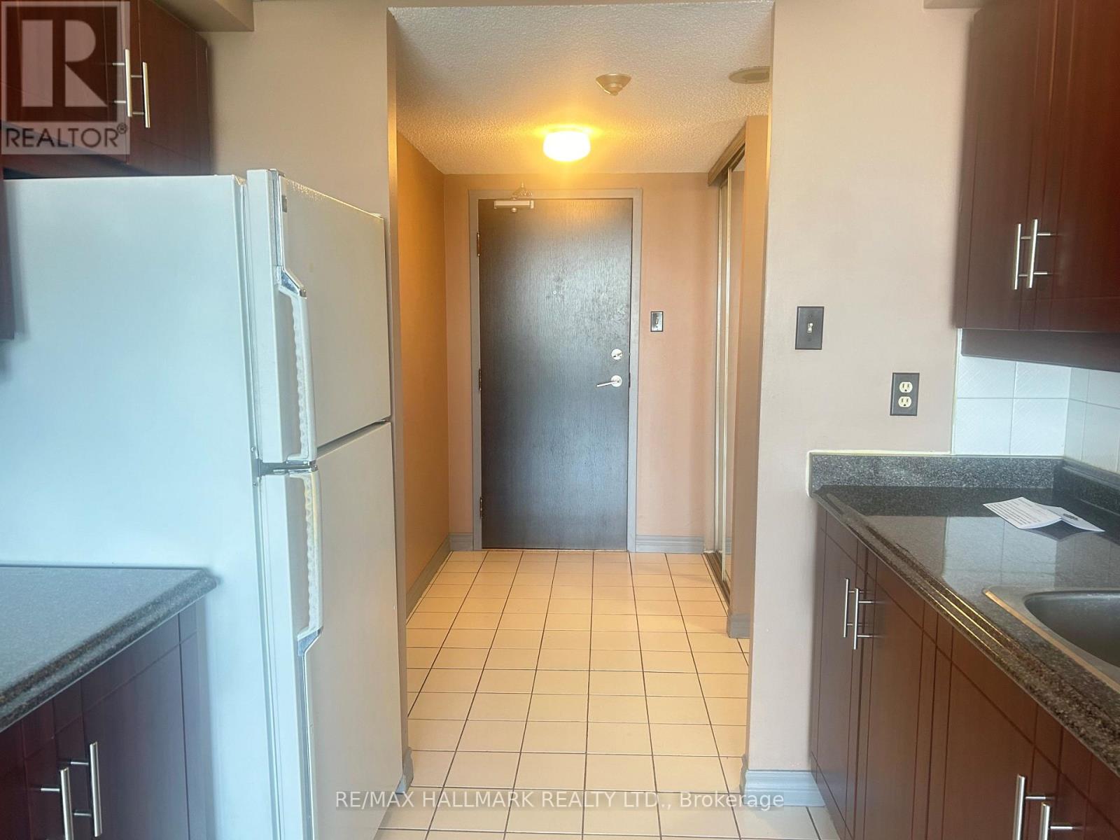 A hallway with a black door and a white refrigerator on the left.