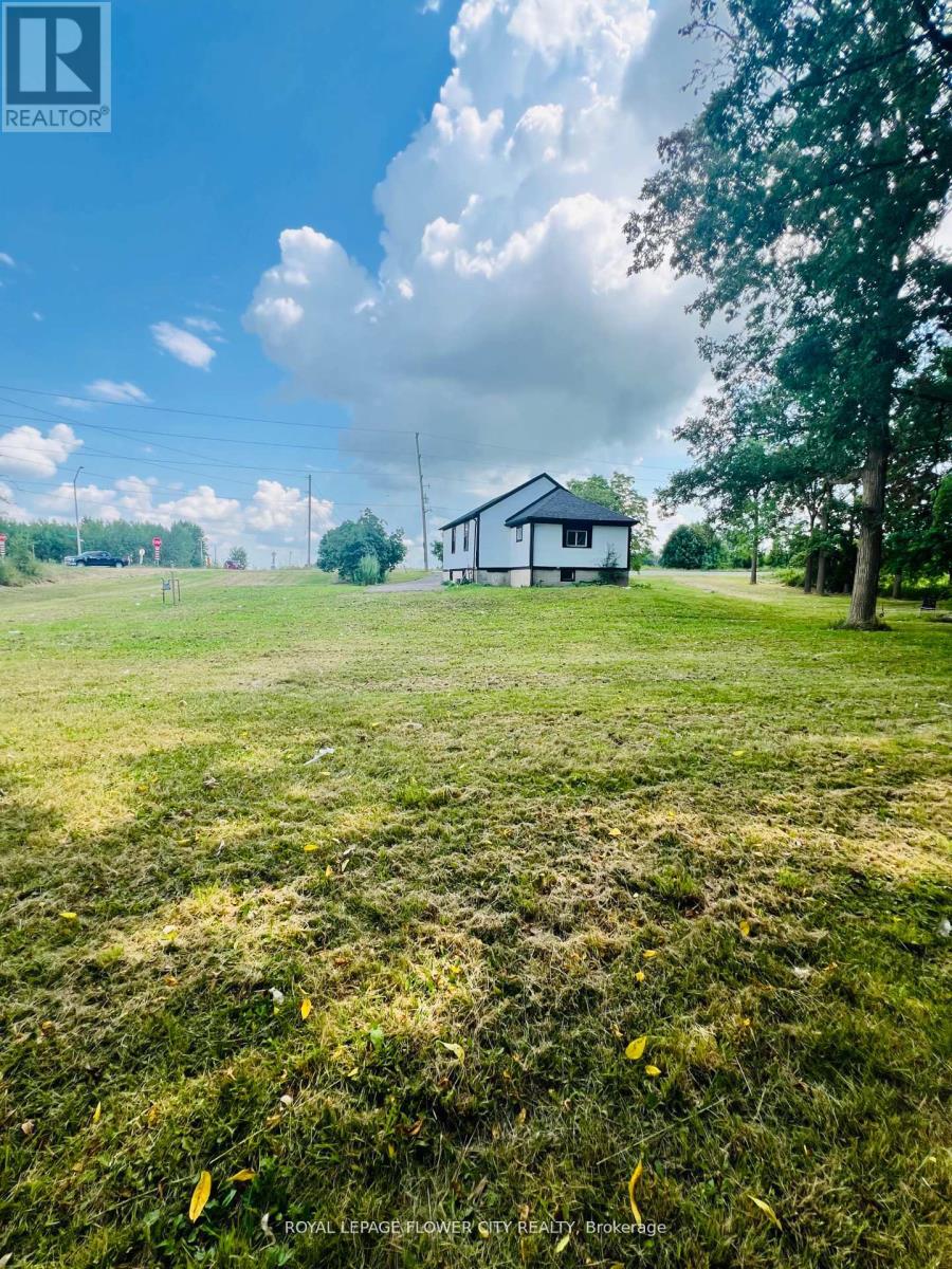 A white house is situated in a grassy field with a tree to the right.