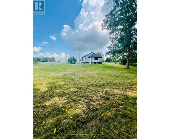 A white house is situated in a grassy field with a tree to the right.