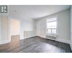 A spacious room with wood flooring and white walls.