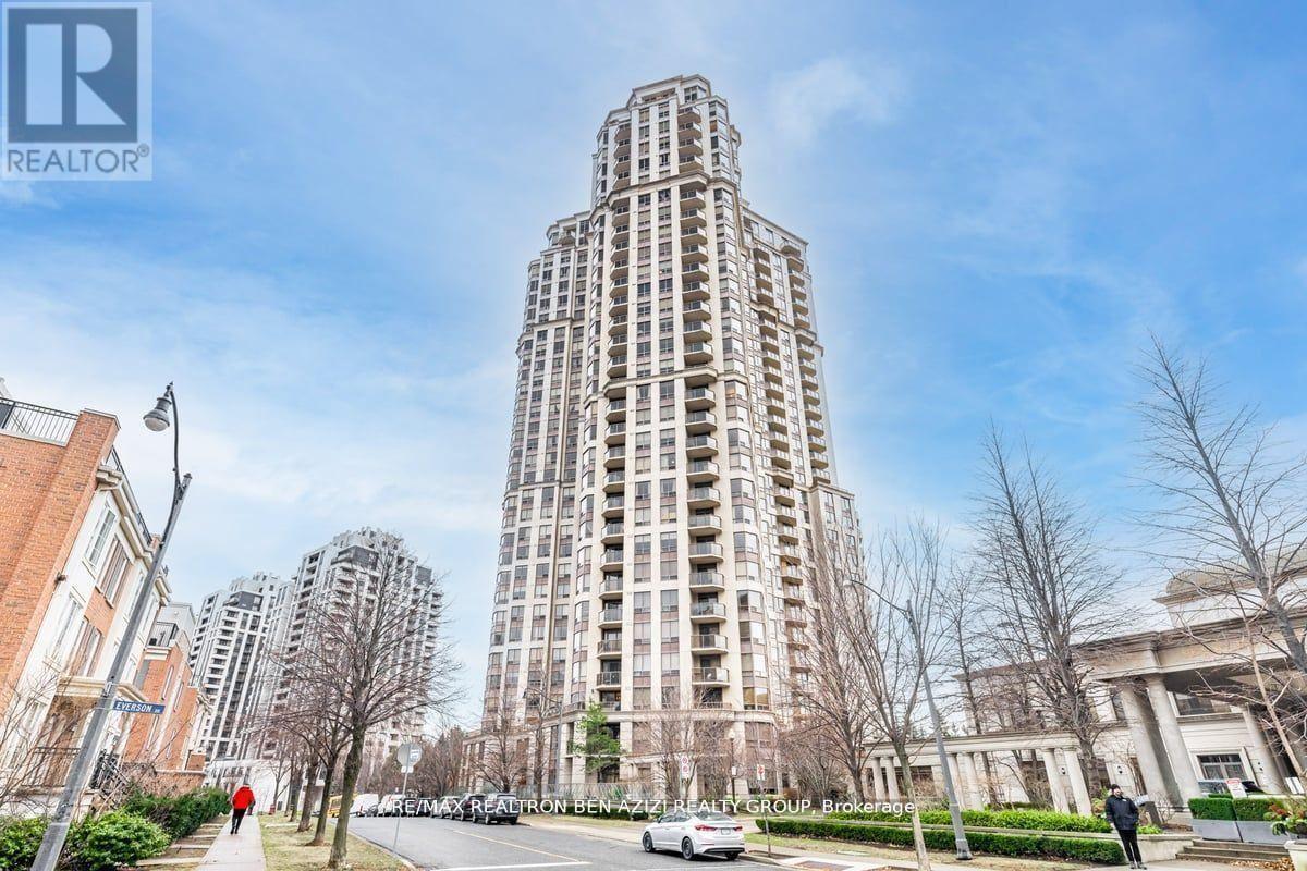 A tall residential building stands in the middle of a street with other buildings in the background.
