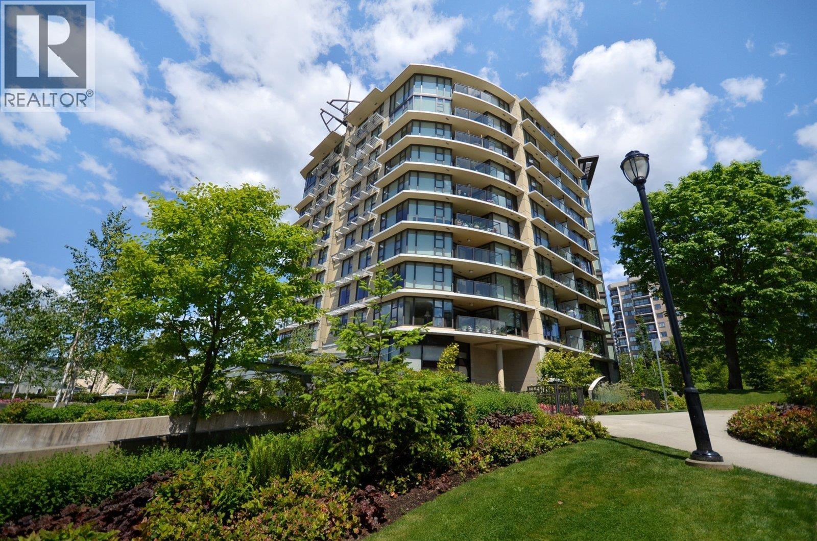A tall residential building with balconies and a green lawn in front.