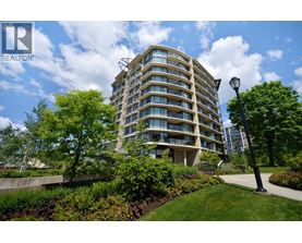 A tall residential building with balconies and a green lawn in front.