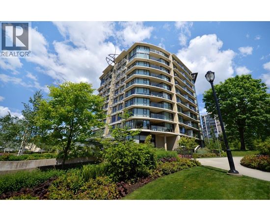 A tall residential building with balconies and a green lawn in front.