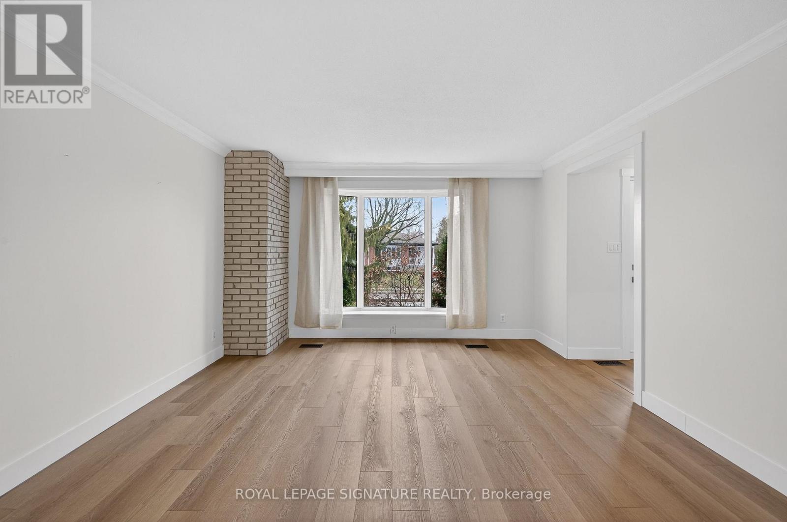 A room with wooden flooring and white walls, with a view of trees through a window.