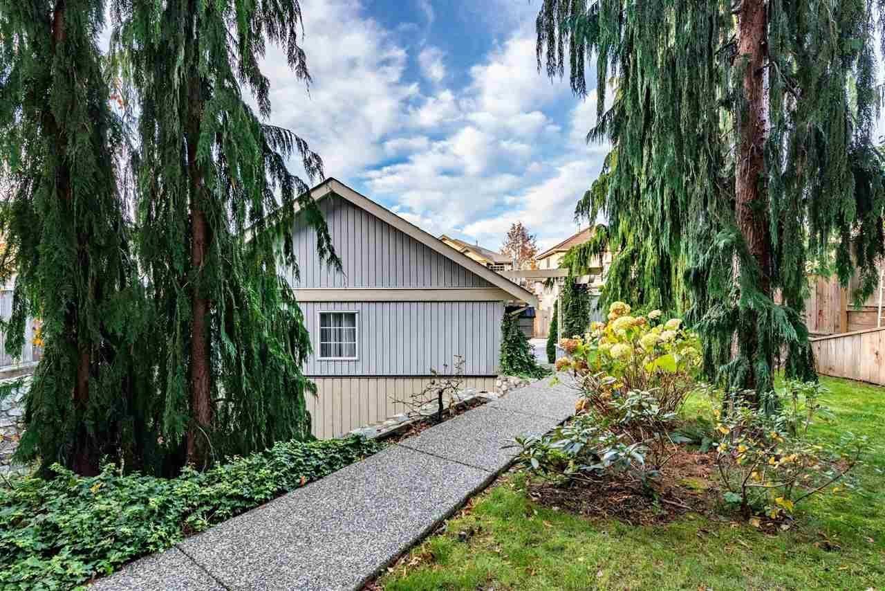 A house with a grey roof and a grey fence is surrounded by green trees.