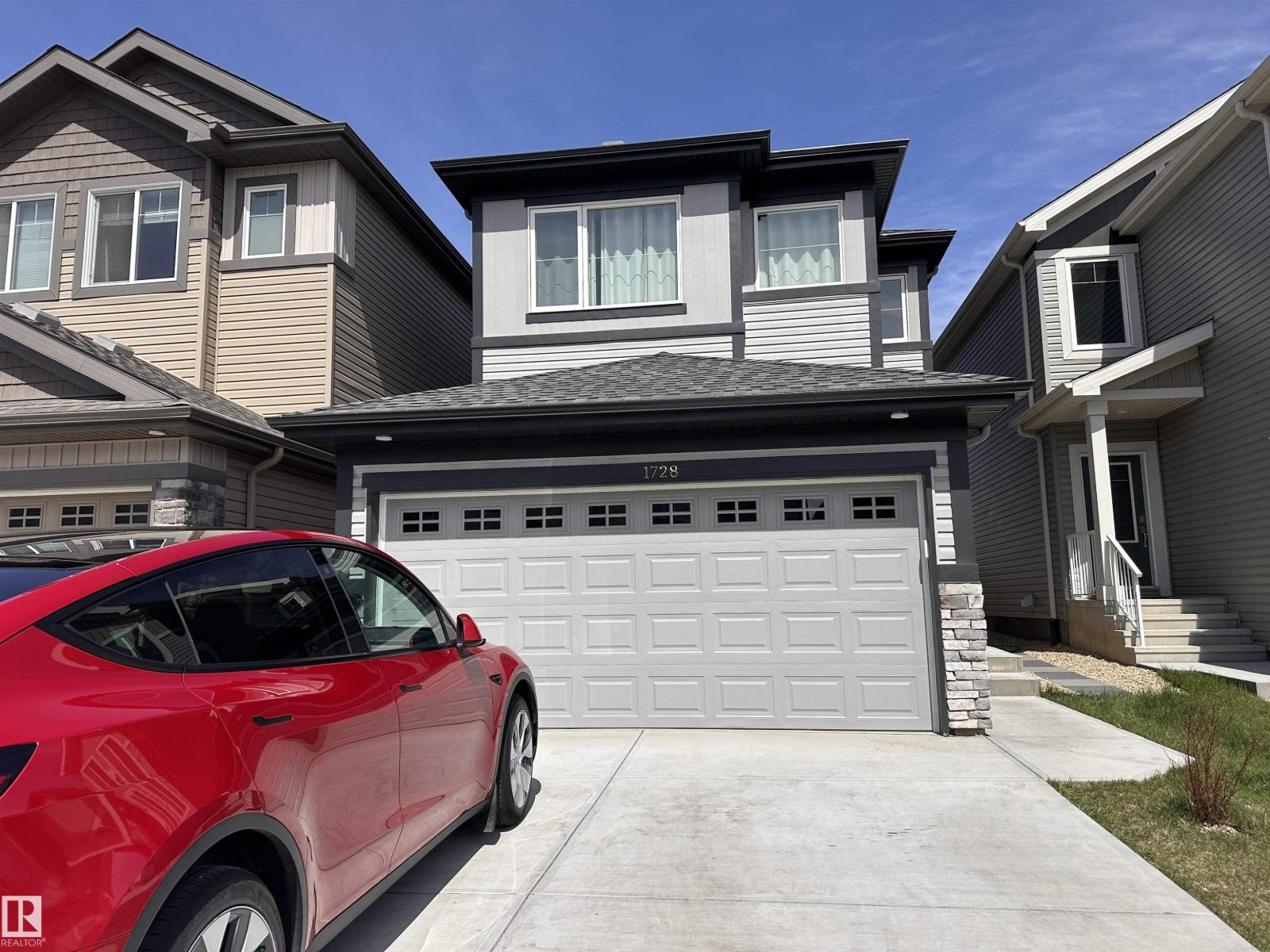 A red car is parked in front of a grey garage.