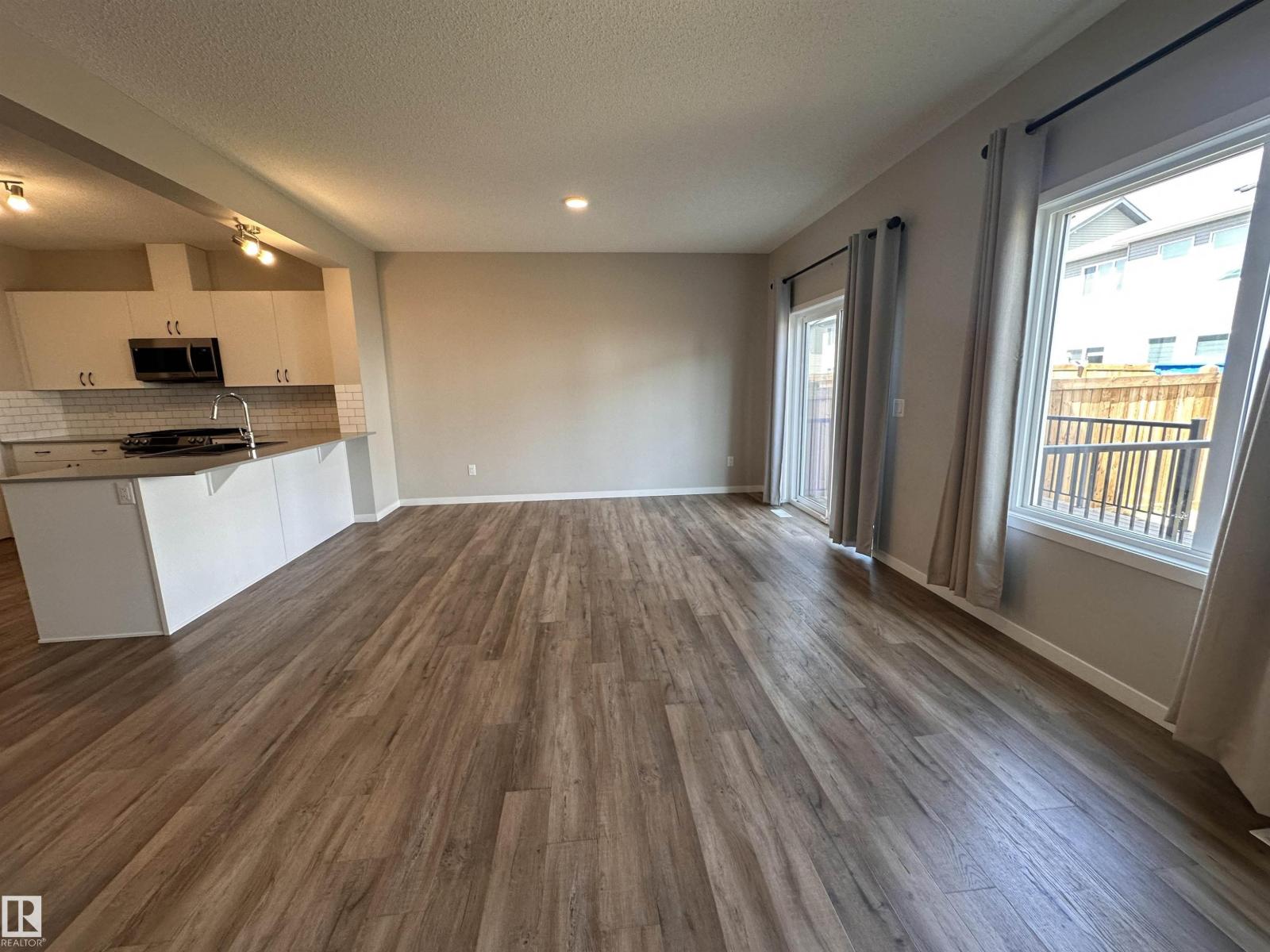 A spacious room with wooden flooring and a window with curtains.
