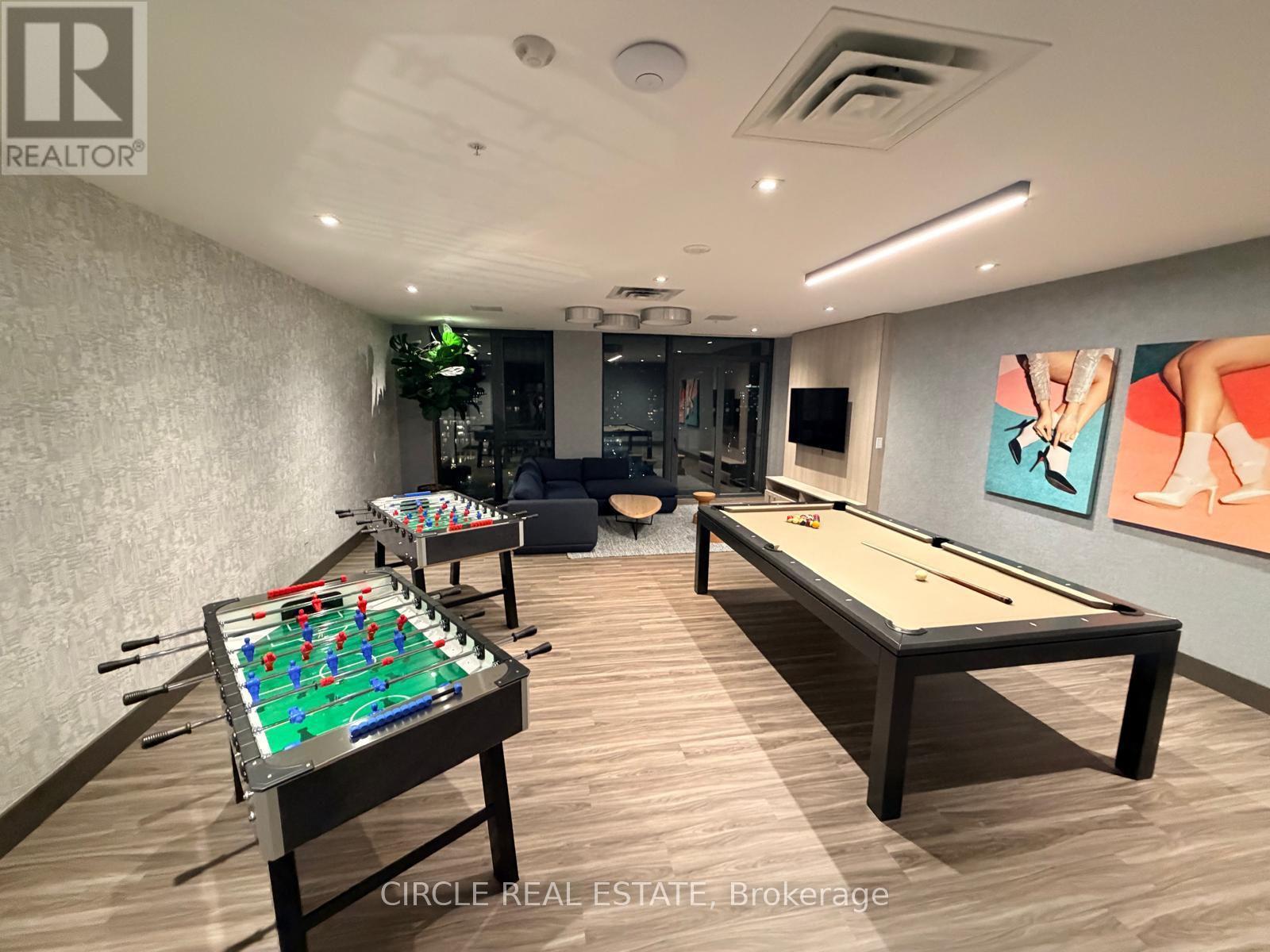 A pool table with a green cloth and a foosball table in a room with a TV and a painting on the wall.