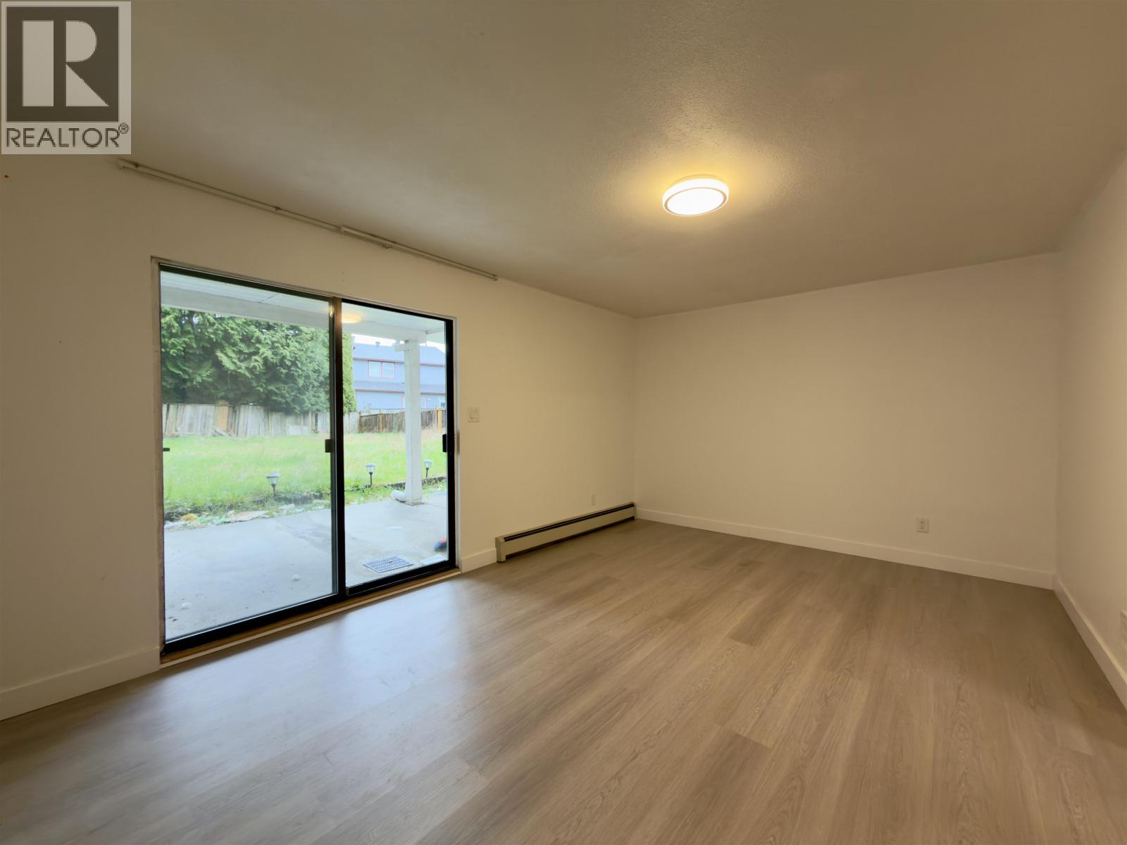 A spacious room with wooden flooring and a sliding glass door leading to a green outdoor area.