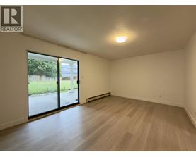 A spacious room with wooden flooring and a sliding glass door leading to a green outdoor area.