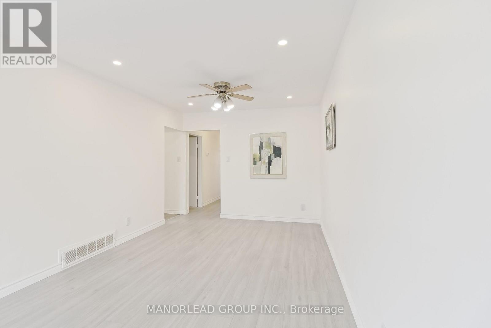 A spacious room with a ceiling fan and a doorway leading to another room.