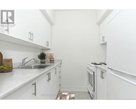 A white kitchen with a sink, stove, and cabinets.
