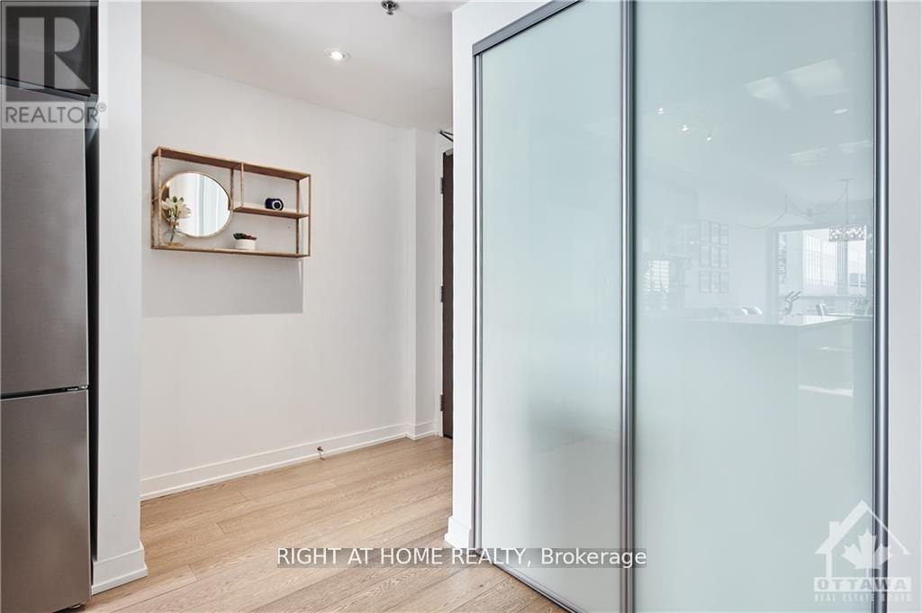 A glass door separates a white room with a wooden floor and a mirrored shelf from a brightly lit space.