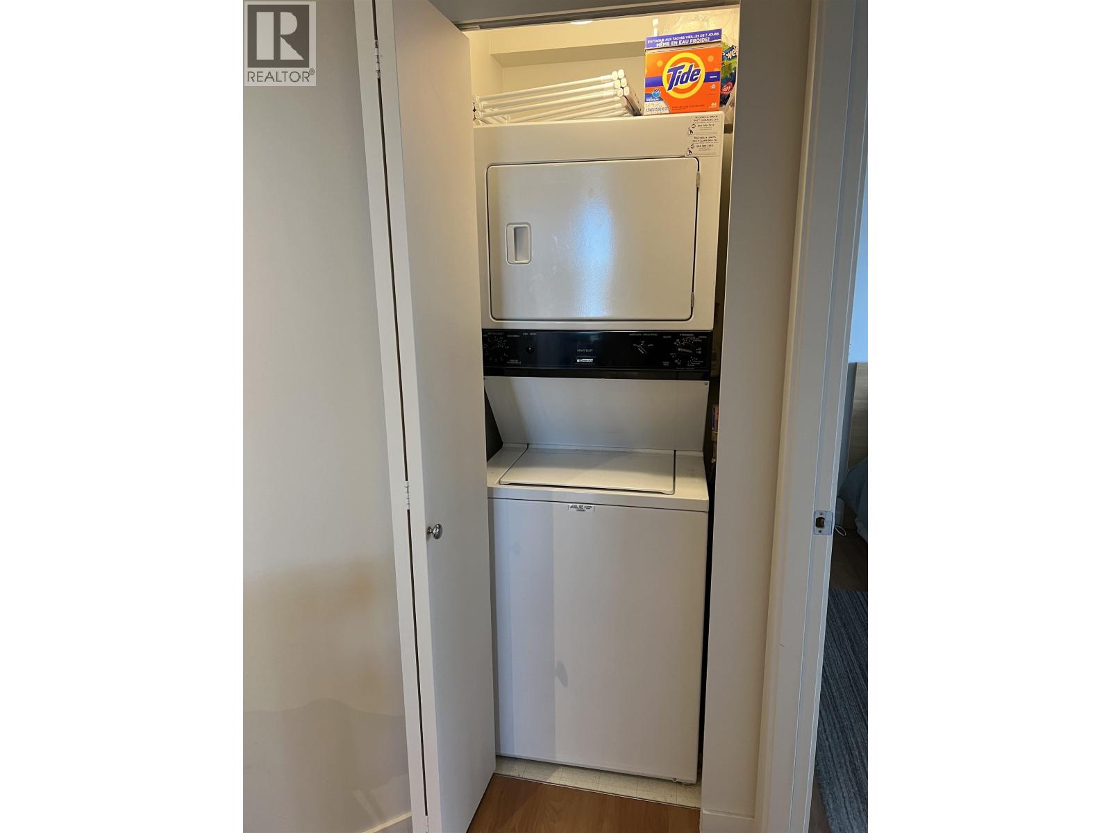 A small white laundry machine sits in a narrow space between a wall and a door.