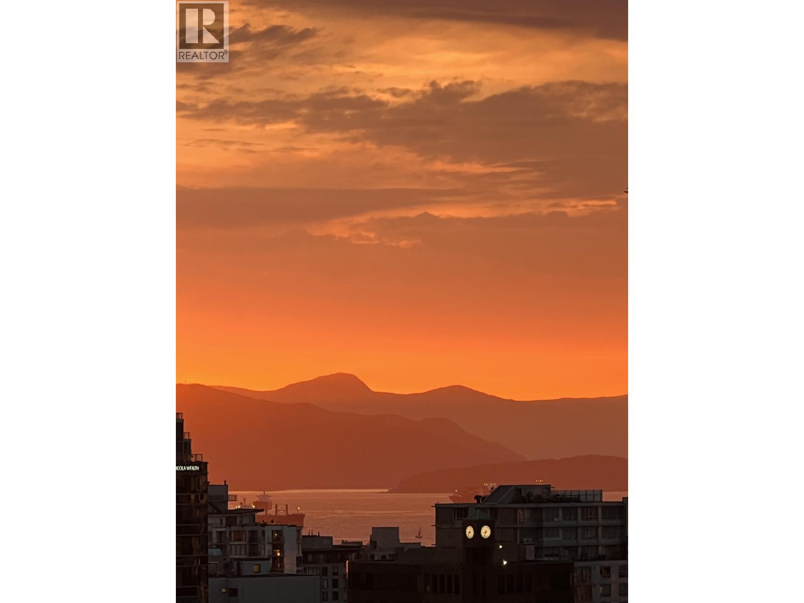 A cityscape with buildings and a body of water under a sunset sky.