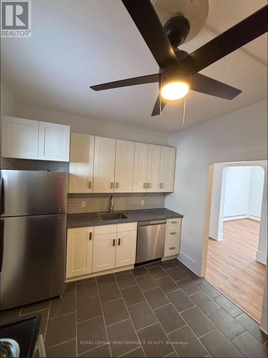 A kitchen with a refrigerator, cabinets, and a ceiling fan.