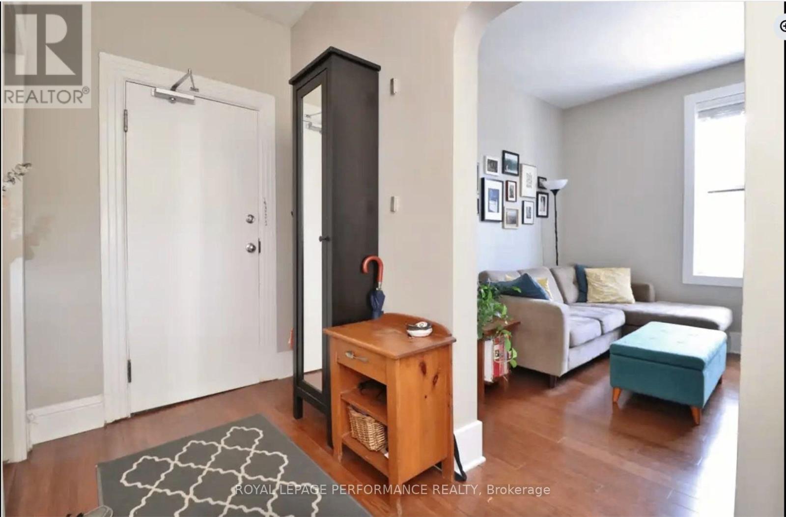 A living room with a white door, a brown cabinet, a grey sofa, and a green ottoman.