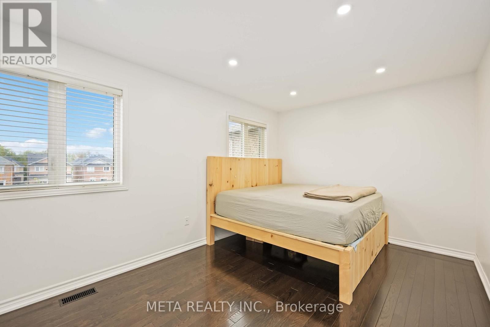 A bedroom with a bed, wooden floors, and a window with blinds.