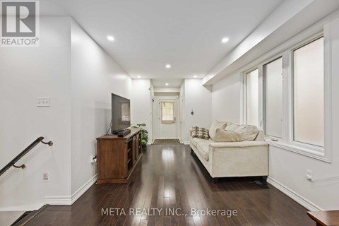 A spacious living room with a white couch and a television on a wooden cabinet.